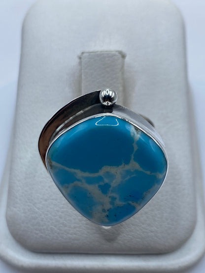 Anillo de plata ajustable con piedra azul cielo en expositor blanco, vista frontal del diseño
