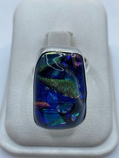 Anillo de plata ajustable con piedra multicolor azul, verde, dorado y violeta en mano de mujer