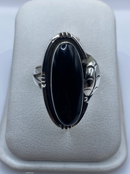 Anillo de plata con ónix negro y manos escultóricas a los lados, vista frontal