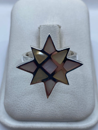 Anillo de plata con forma de estrella de ocho puntas y piedras multicolor engastadas, visto de frente sobre fondo blanco