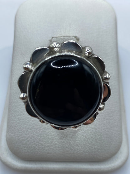Anillo de plata con onix negro y flores en relieve, visto desde arriba sobre fondo blanco
