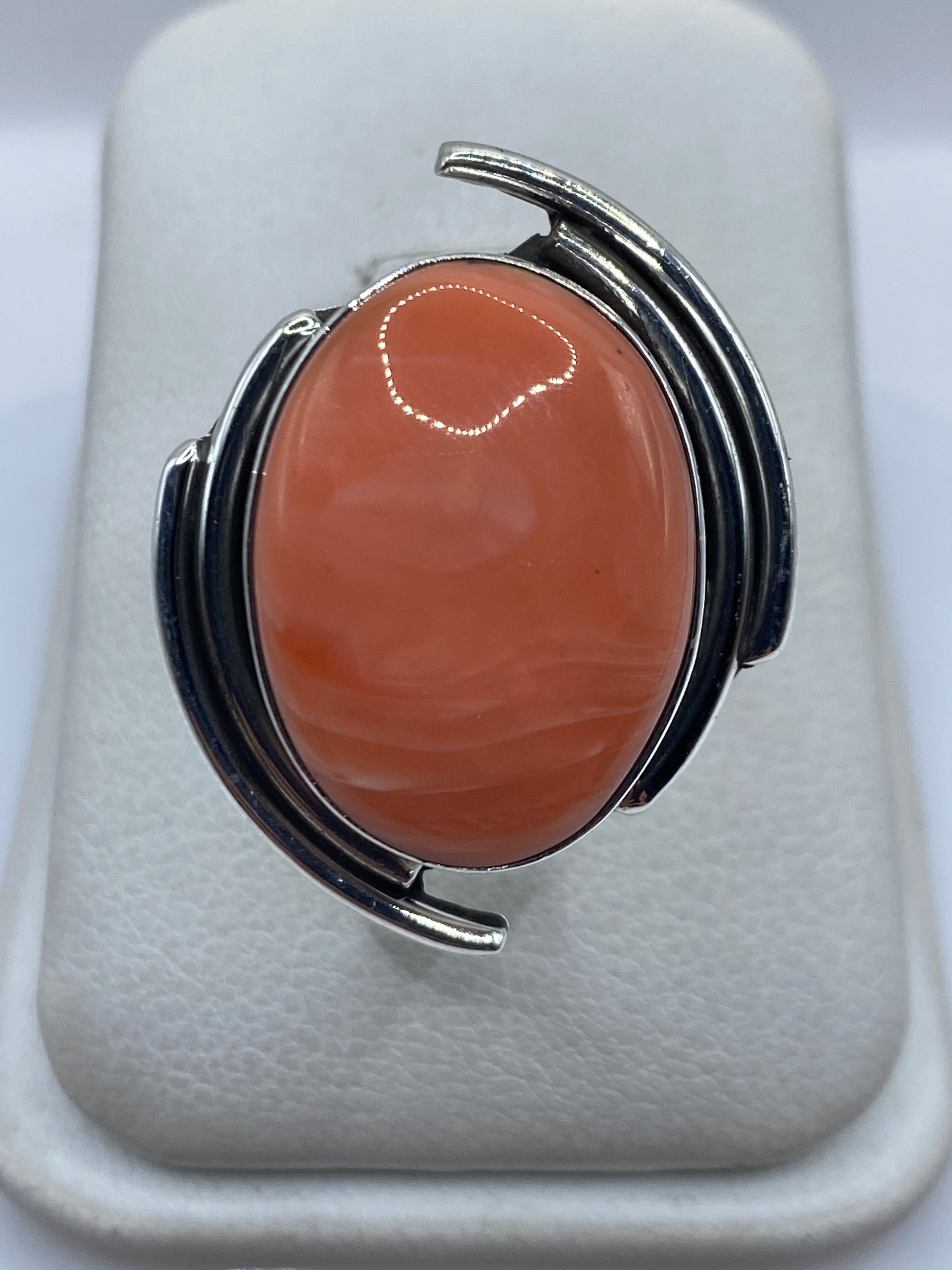 Anillo de plata escultural con coral naranja rojizo visto de frente en la mano