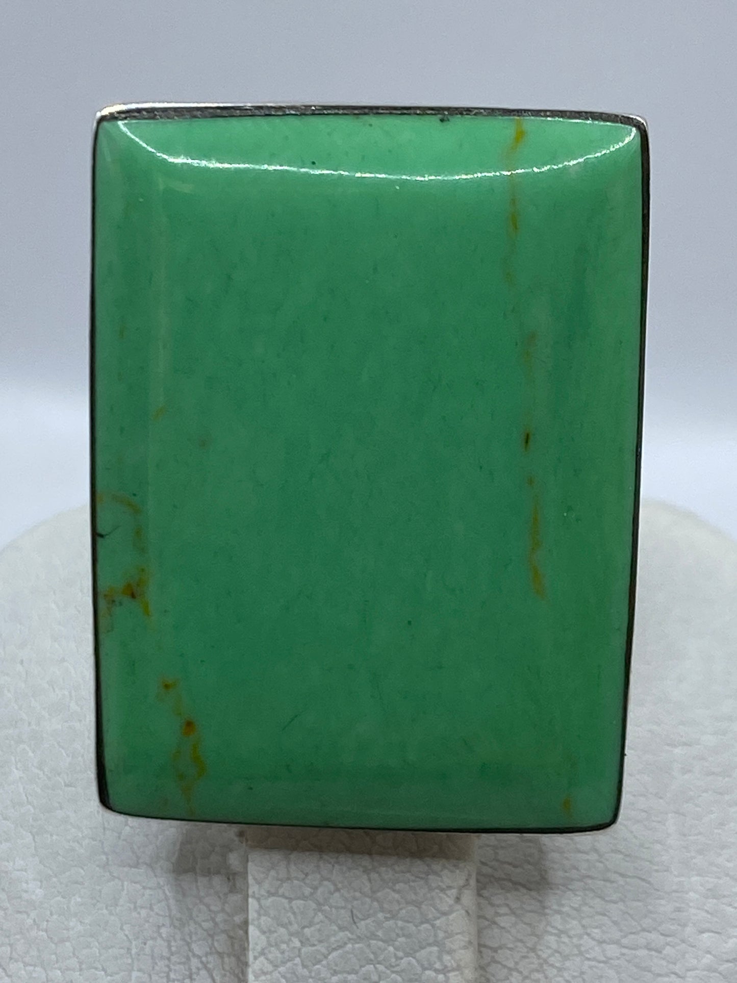 Anillo de plata con piedra verde sobre dedo, con luz natural