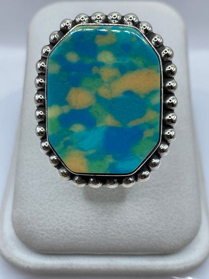 Anillo de plata con incrustación de piedra multicolor (azul, verde, amarillo) en la mano de una mujer