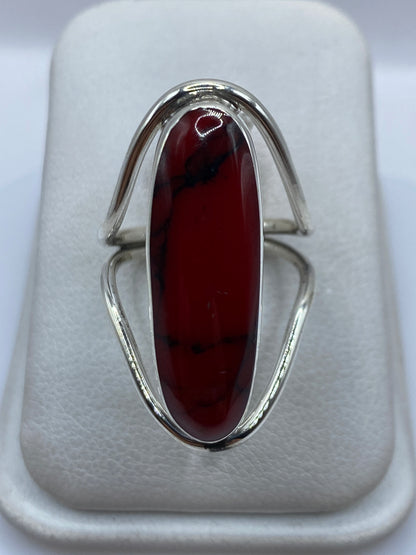 Anillo de plata con coral rojo ovalado en la mano, vista frontal