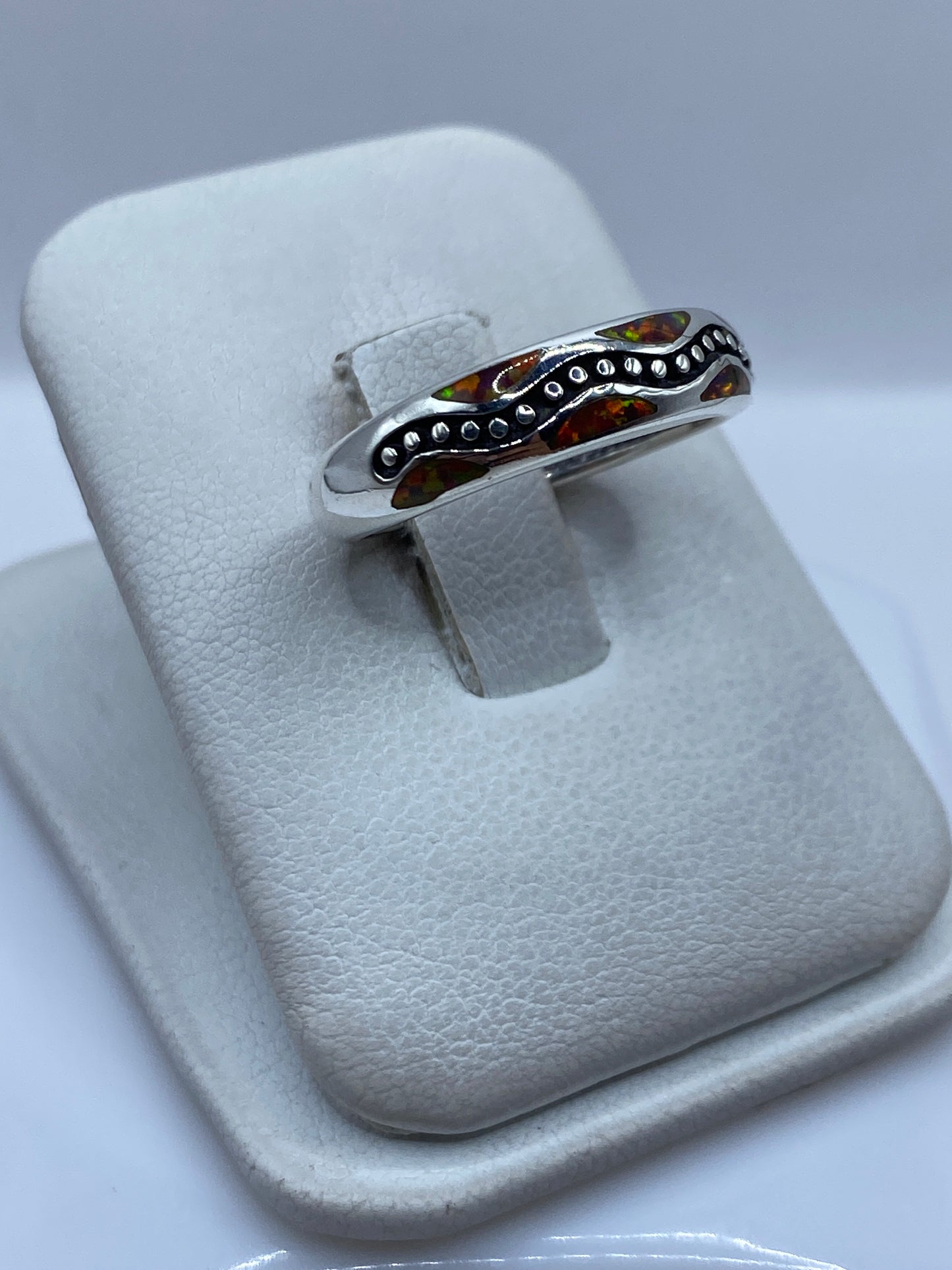 Anillo de ópalo multicolor en la mano, mostrando los tonos rojos, naranjas y amarillos