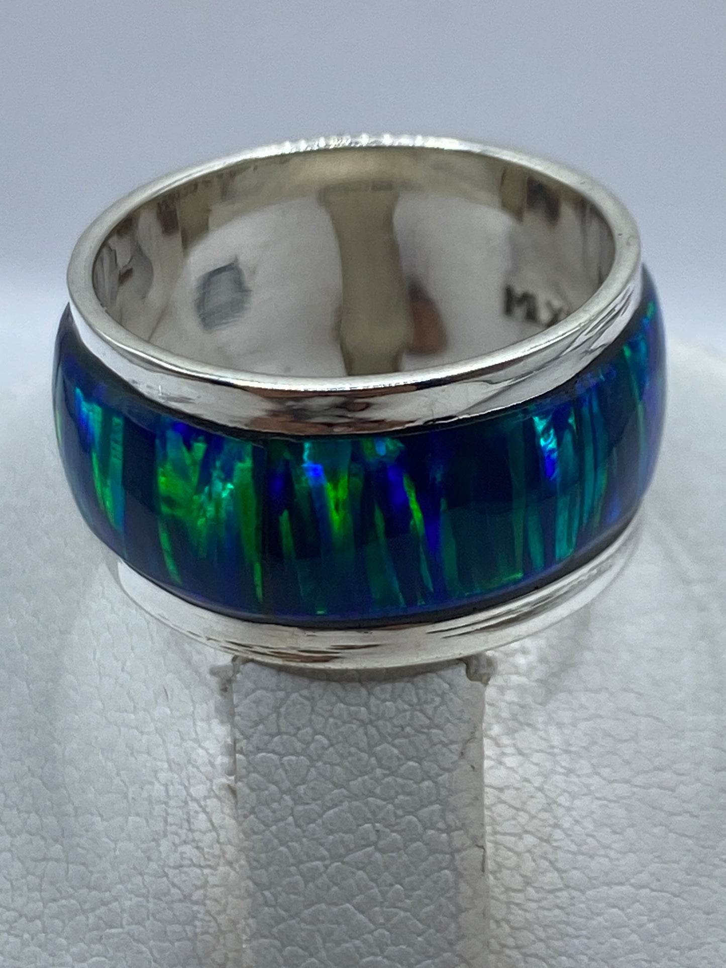 Anillo en dedo, mostrando el reflejo azul verdoso del ópalo y el acabado pulido de la banda