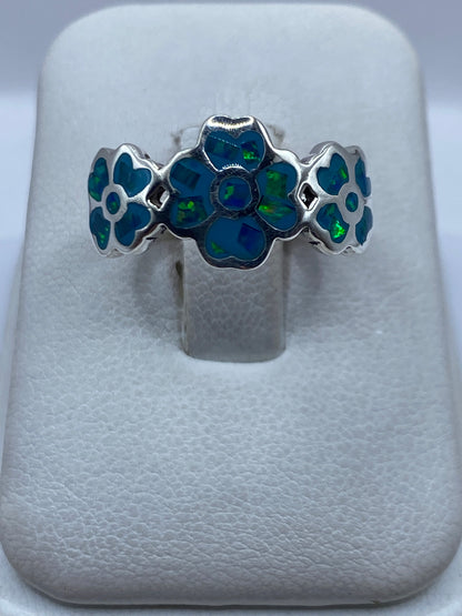 Anillo de plata con flores y ópalo de fuego azul cielo, vista frontal en estuche blanco