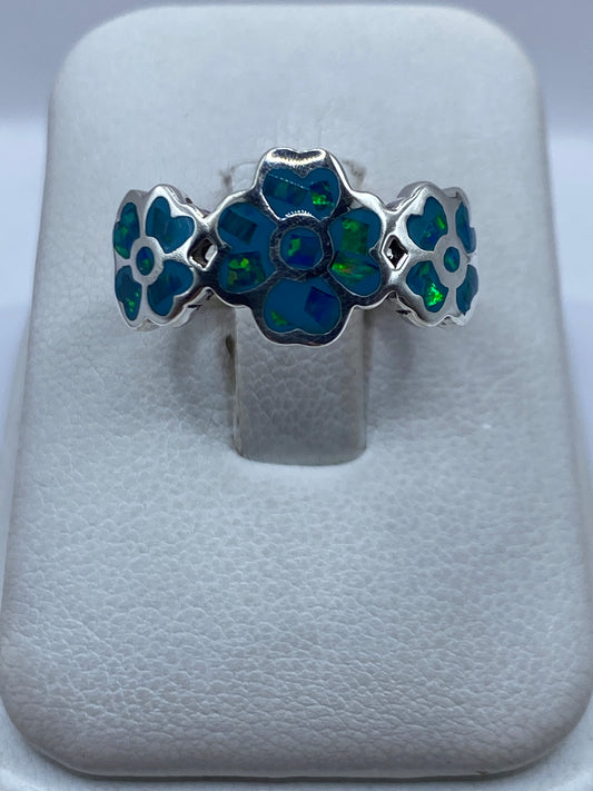 Anillo de plata con flores y ópalo de fuego azul cielo, vista frontal en estuche blanco