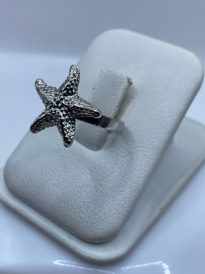 Anillo estrella marina de plata en la mano de una mujer, mostrando el relieve del diseño