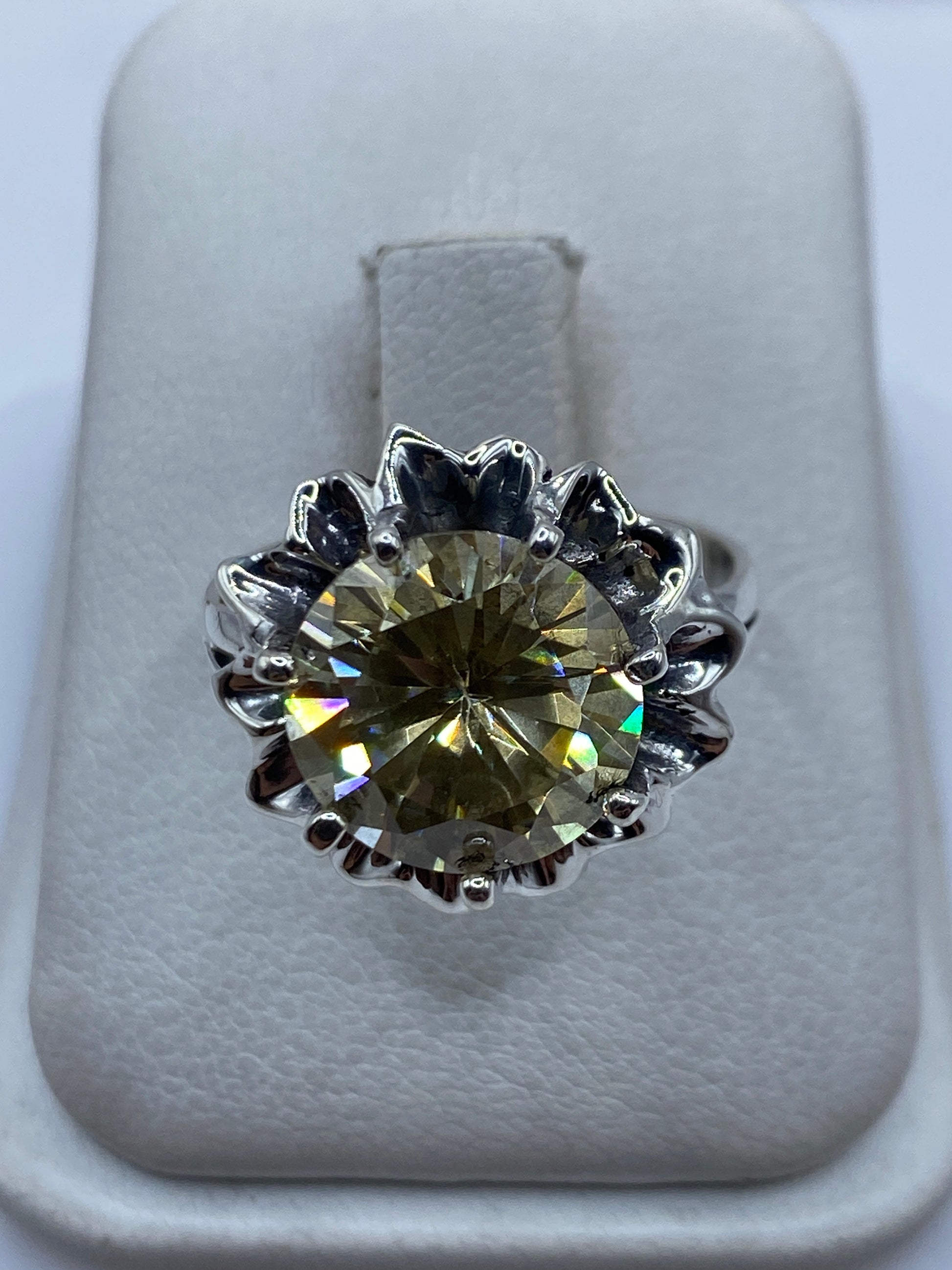 Anillo de plata .925 con circonia amarillo verdoso engastada en corona floral, visto de frente en estuche blanco