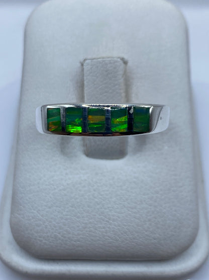 Anillo de plata con cinco ópalos de fuego verde limón engastados en fila sobre fondo blanco