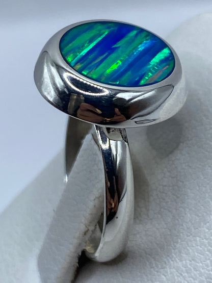 Anillo de plata con ópalo de fuego puesto en dedo, luz natural iluminando el brillo iridiscente