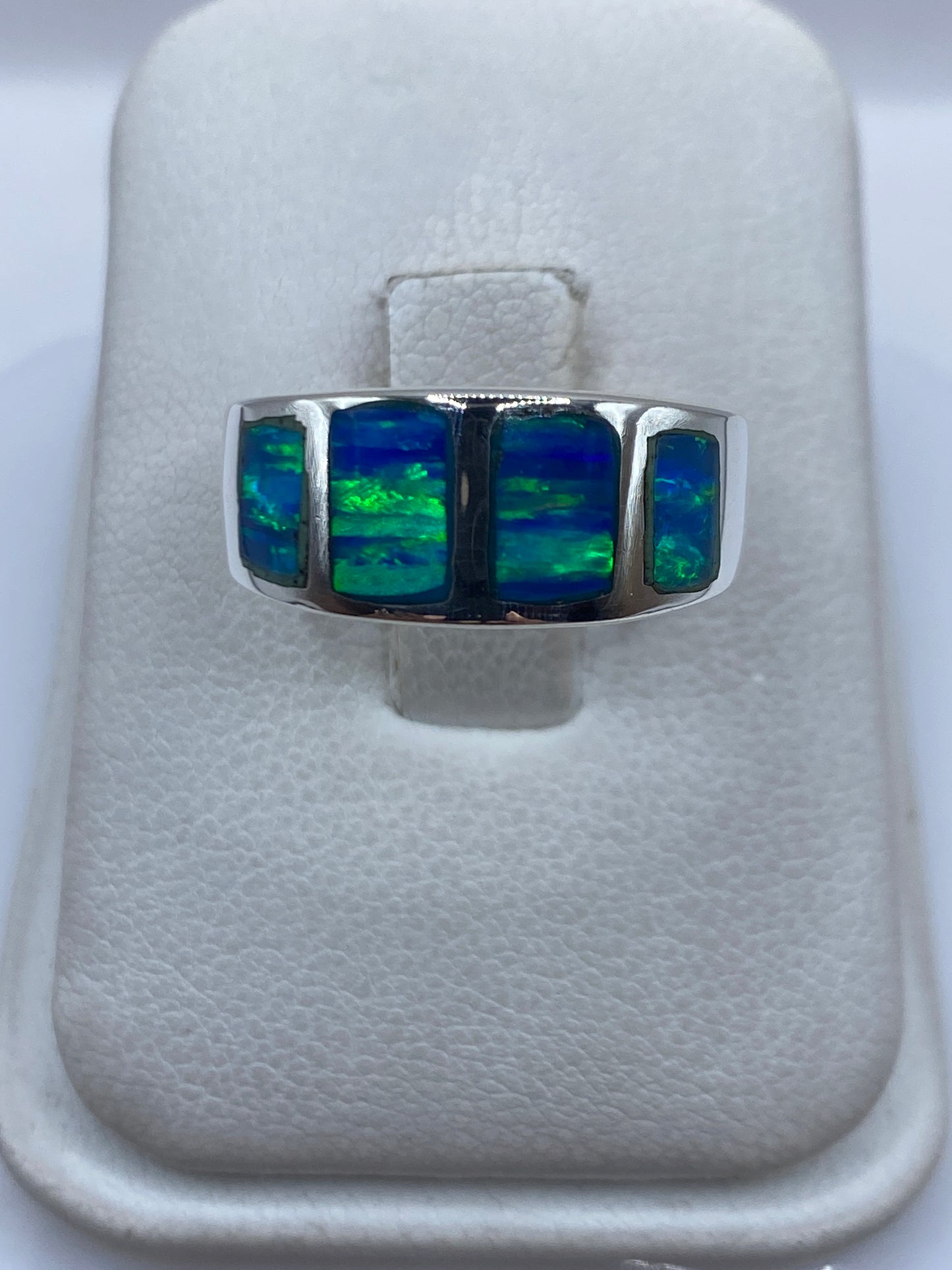 Anillo de plata .925 con ópalo de fuego azul engastado a mano, sobre dedo, mostrando destellos verdes