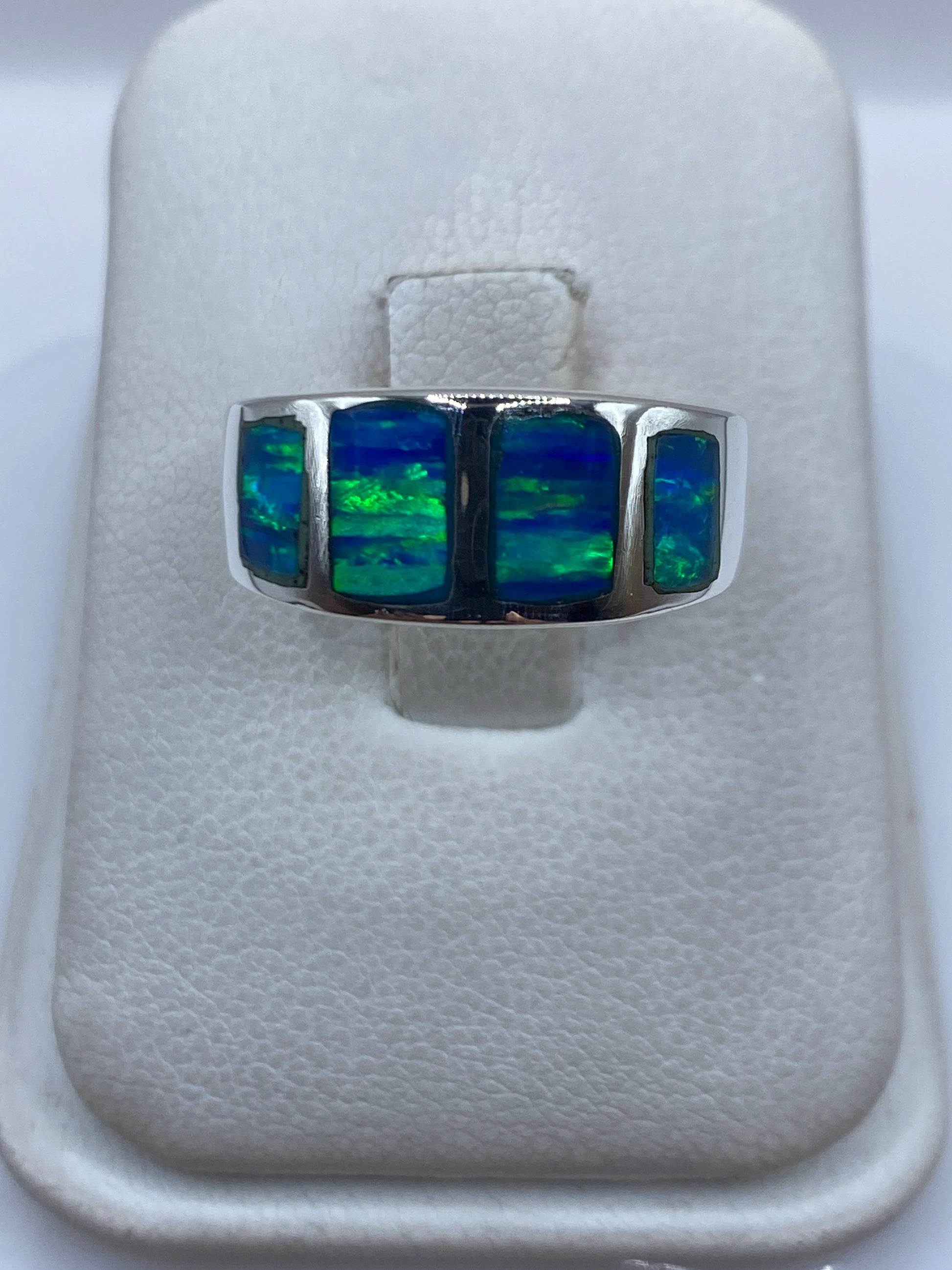 Anillo de plata .925 con ópalo de fuego azul engastado a mano, sobre dedo, mostrando destellos verdes