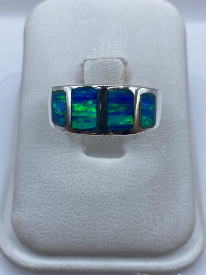 Anillo de plata .925 con ópalo de fuego azul engastado a mano, sobre dedo, mostrando destellos verdes