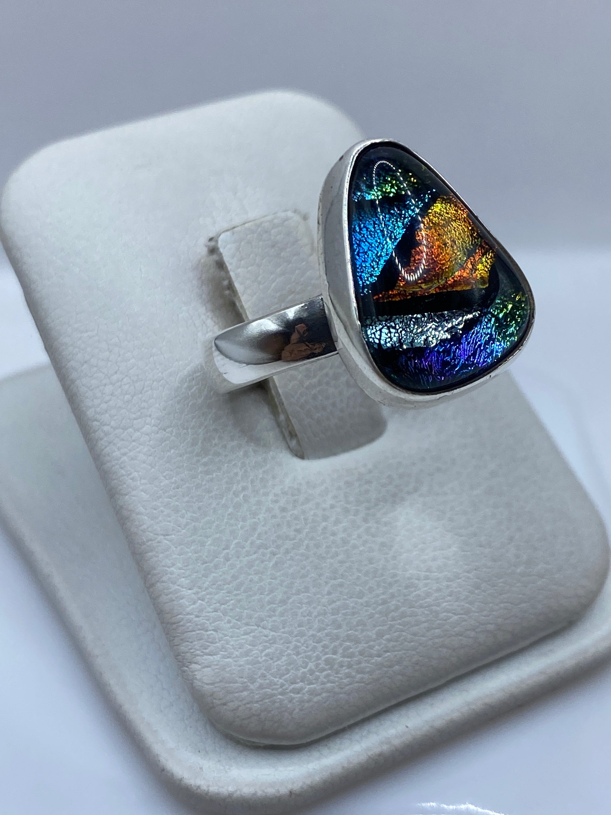 Detalle del anillo con piedra reflejando azules, dorados y reflejos iridiscentes