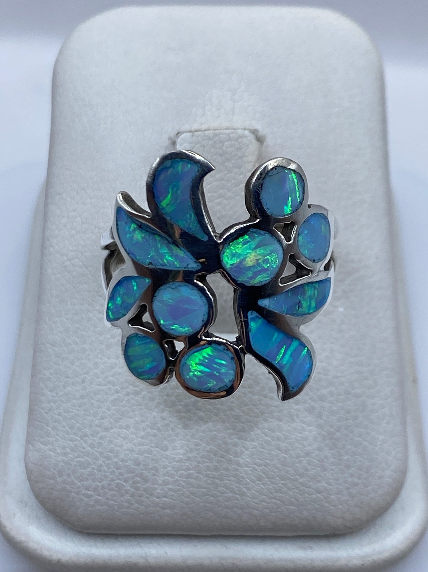 Anillo de plata con ópalo de fuego azul cielo iridiscente en diseño floral, sobre cojín blanco