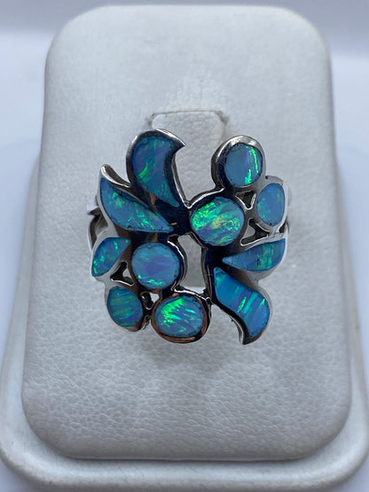 Anillo de plata con ópalo de fuego azul cielo iridiscente en diseño floral, sobre cojín blanco
