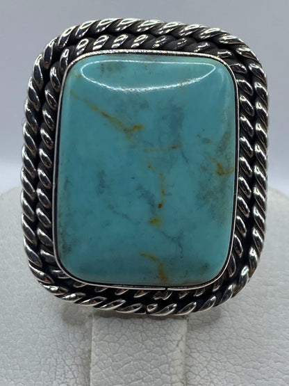 Anillo en dedo portando turquesa azul cielo y marco de plata retorcido de Taxco