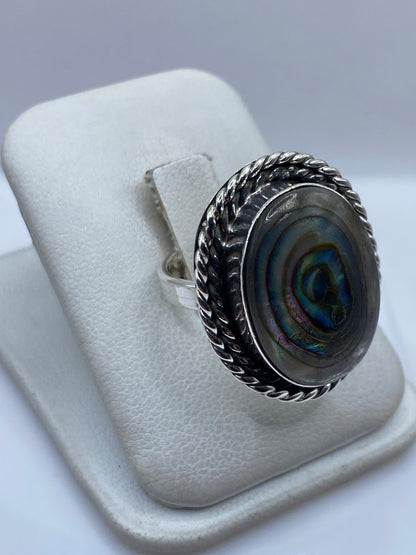 Vista frontal del anillo con piedra oval engastada, mostrando tonos verdes y azules