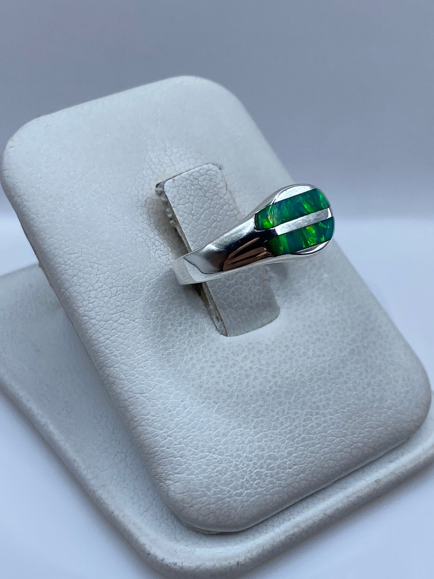 Anillo de plata ópalo fuego verde en dedo, mostrando los reflejos luminosos de la piedra