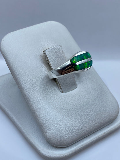 Anillo de plata ópalo fuego verde en dedo, mostrando los reflejos luminosos de la piedra