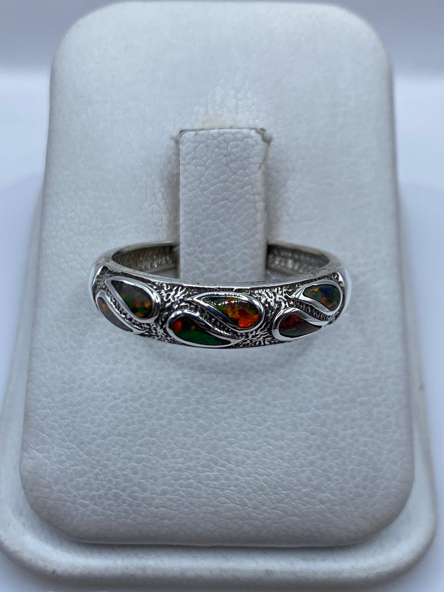 Anillo de plata .950 con ópalo de fuego multicolor engastado en la mano, mostrando los tonos verdes, rojos y naranjas
