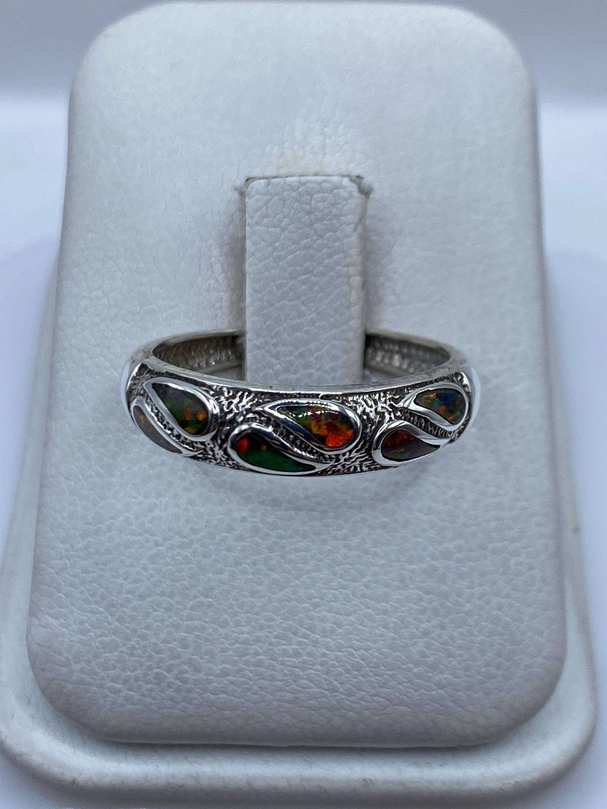 Anillo de plata .950 con ópalo de fuego multicolor engastado en la mano, mostrando los tonos verdes, rojos y naranjas