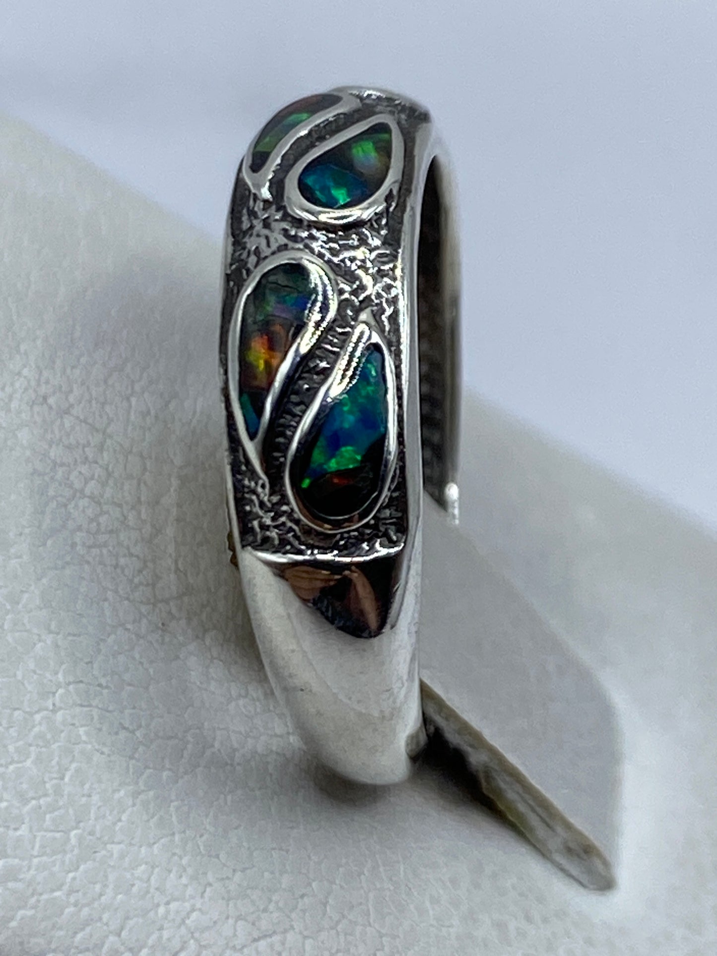 Anillo de ópalo de fuego en dedo, mostrando los tonos dorados y azules cambiantes