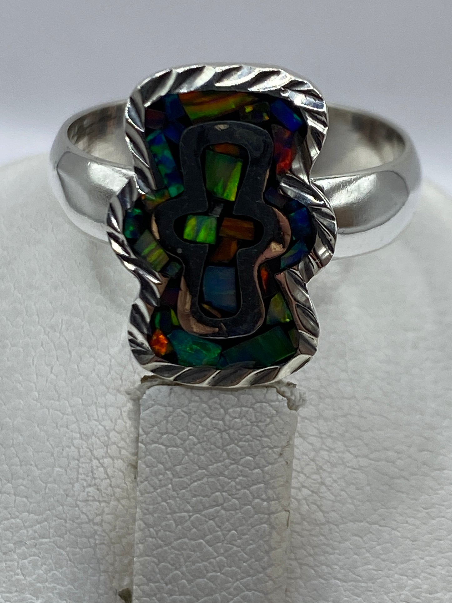 Anillo puesto en dedo mostrando los reflejos verdes, azules y naranjas del ópalo