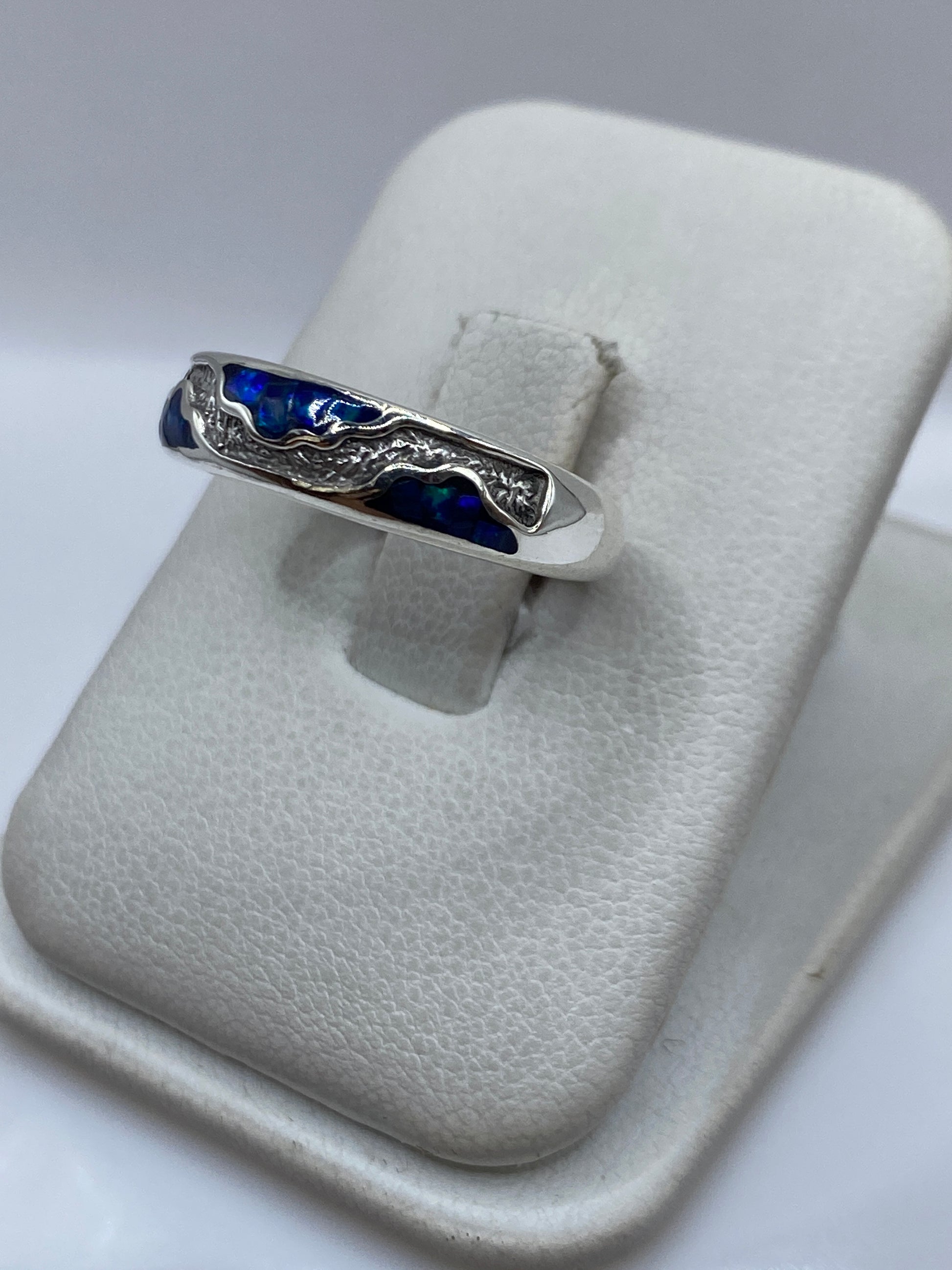 Detalle lateral del anillo de ópalo azul sobre dedo, mostrando la profundidad del color