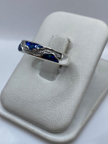Detalle lateral del anillo de ópalo azul sobre dedo, mostrando la profundidad del color