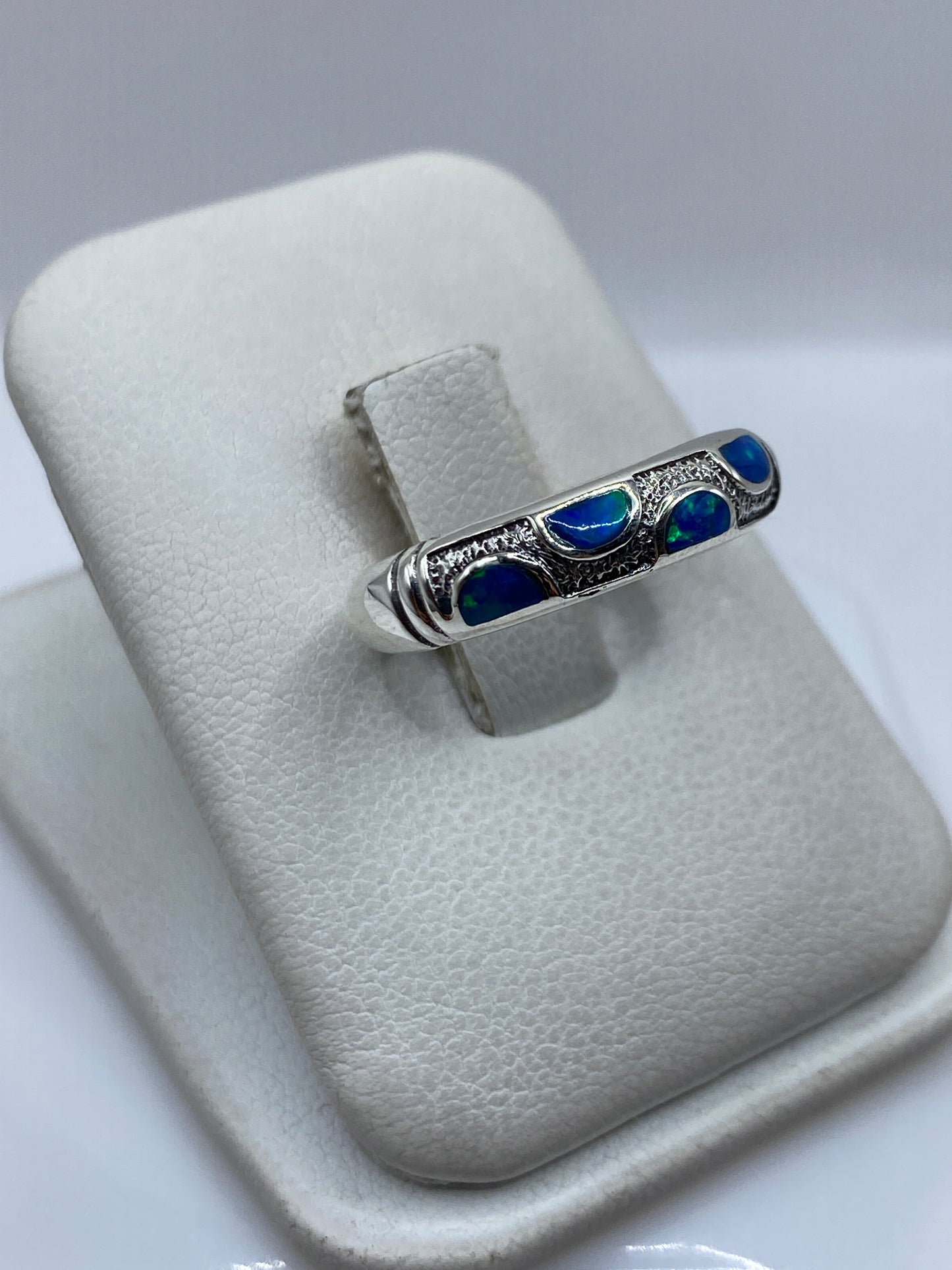 Anillo de plata ópalo de fuego azul desde el lateral, mostrando el engaste a mano y la forma curva