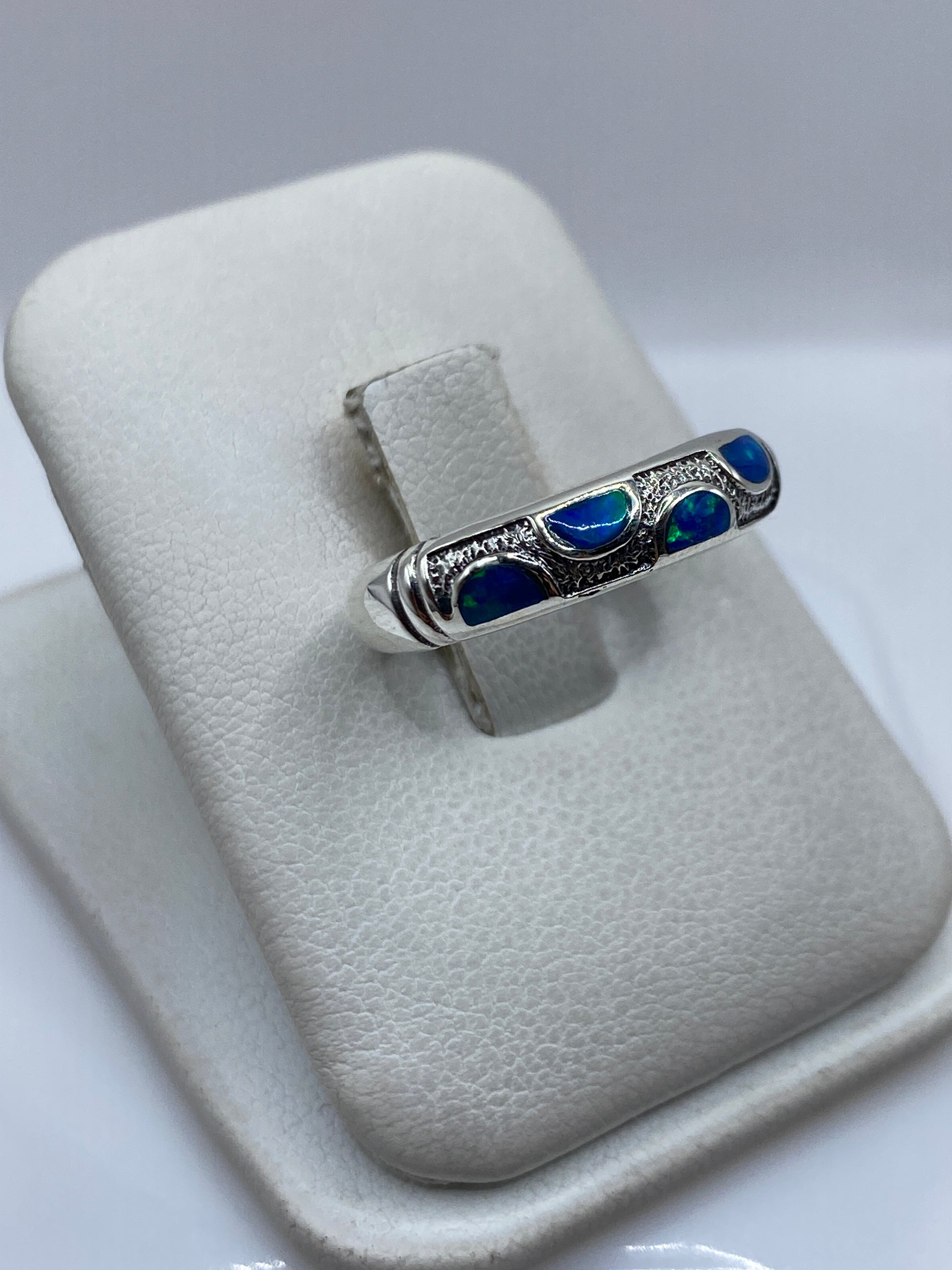 Anillo de plata ópalo de fuego azul desde el lateral, mostrando el engaste a mano y la forma curva