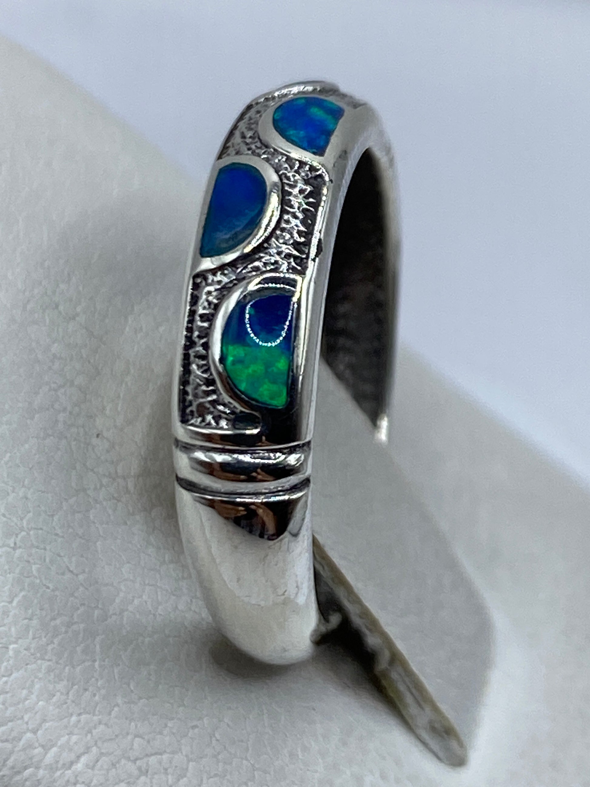 Anillo de ópalo de fuego azul en dedo unisex, con luz natural resaltando los tonos profundos