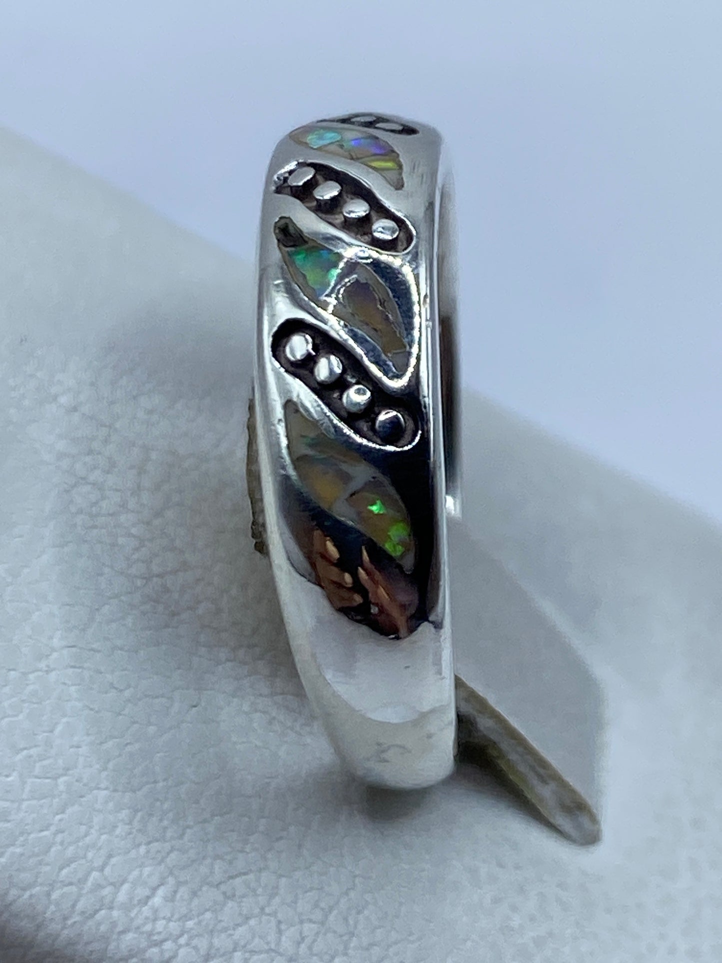 Anillo llevado en el dedo mostrando el ópalo brillante con tonos verdes, azules y naranjas