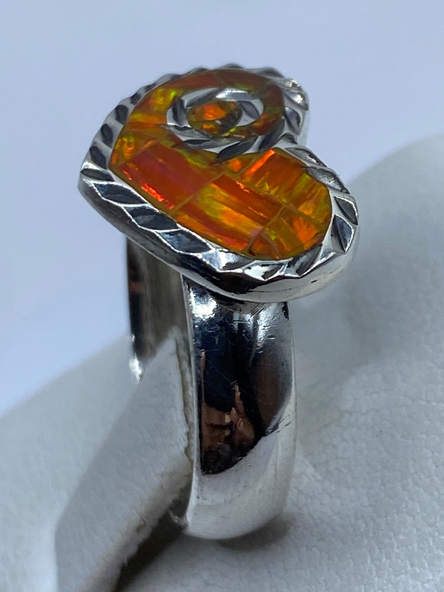 Anillo de corazón sobre dedo mostrando los tonos naranjas brillantes del ópalo