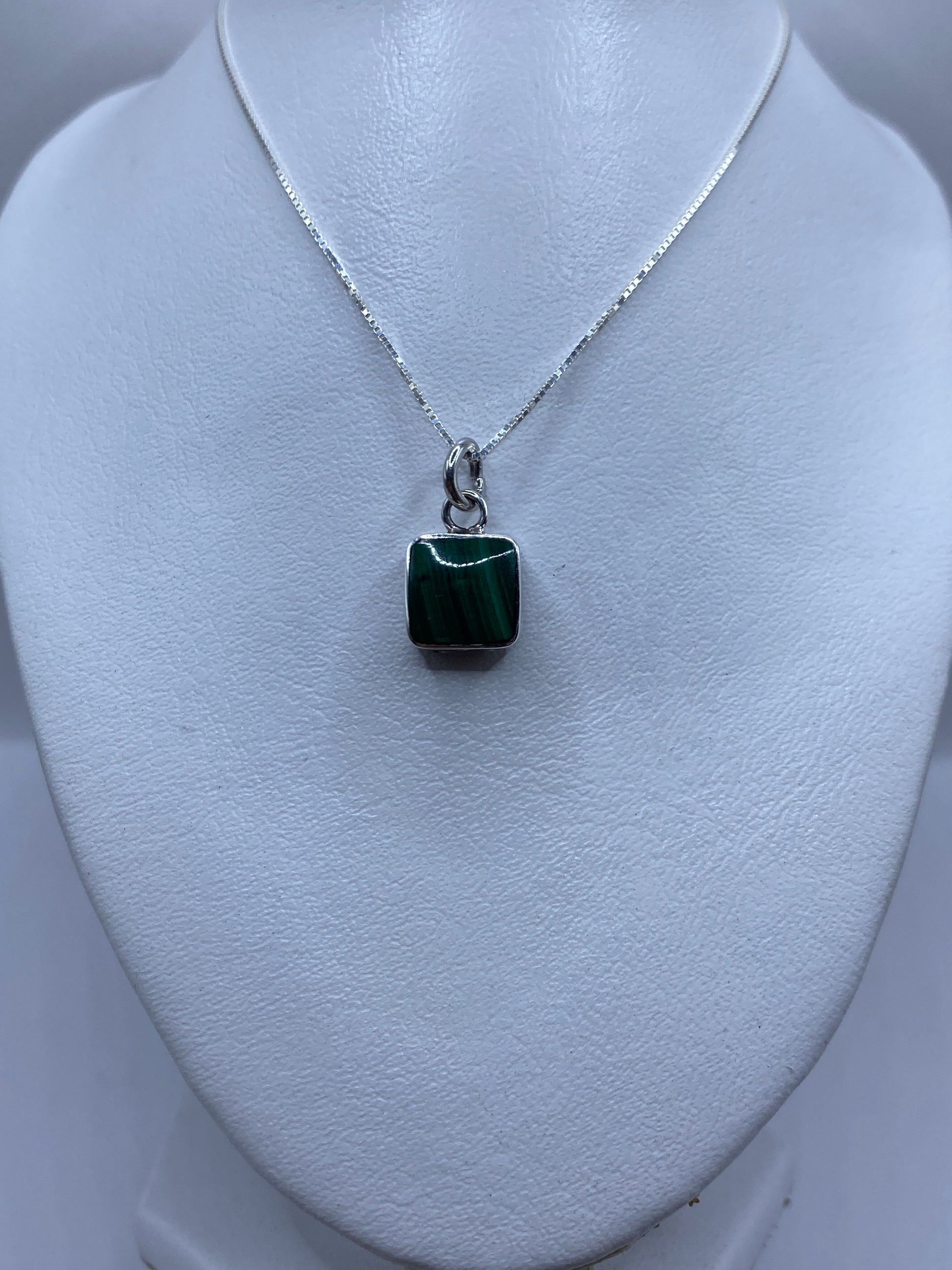 Dije sobre fondo blanco mostrando el contraste de plata pulida y piedra verde