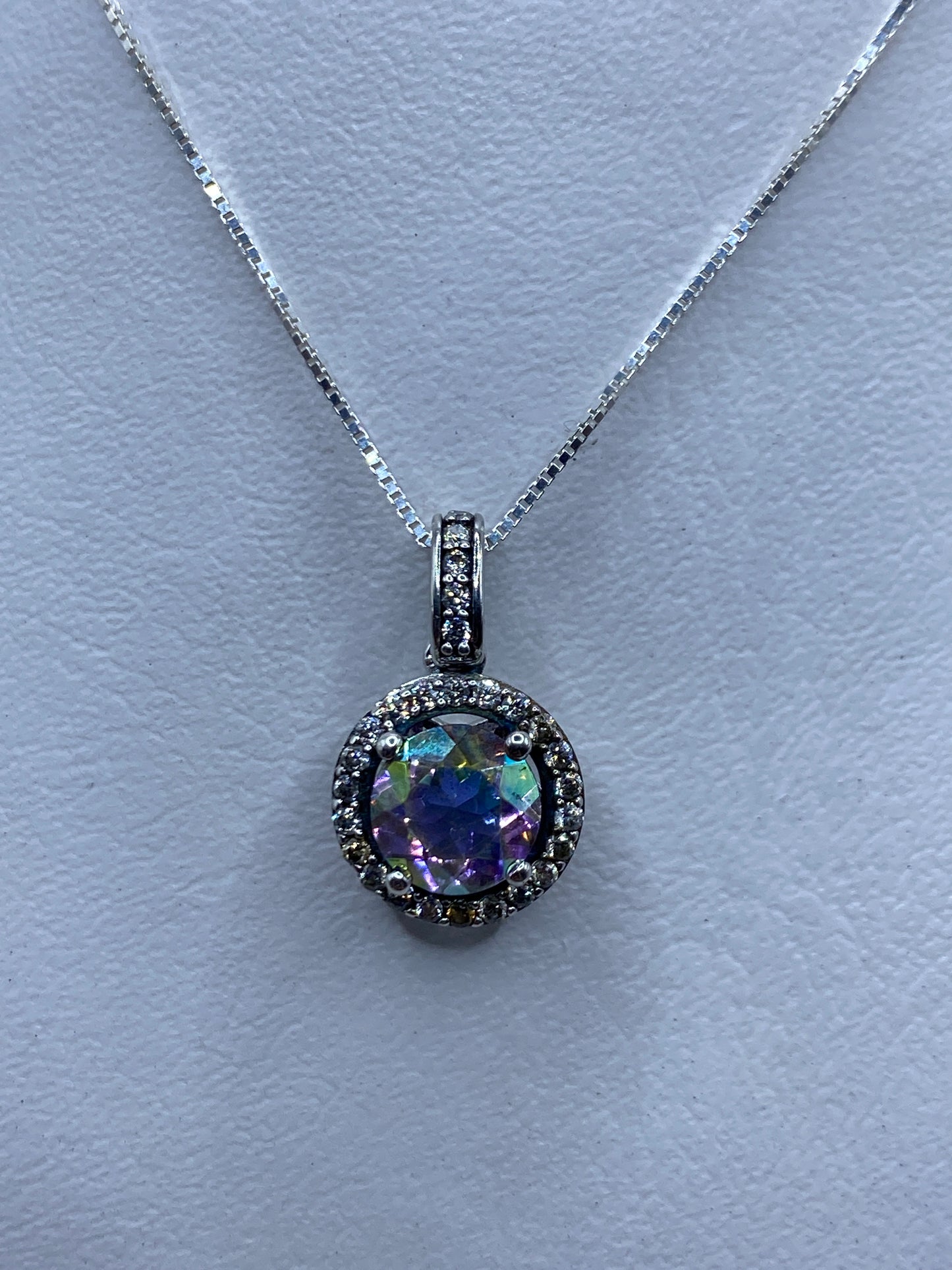 Dije de plata con circonia multicolor facetada, colgado de cadena, reflejando luz en tonos púrpura, verde y azul