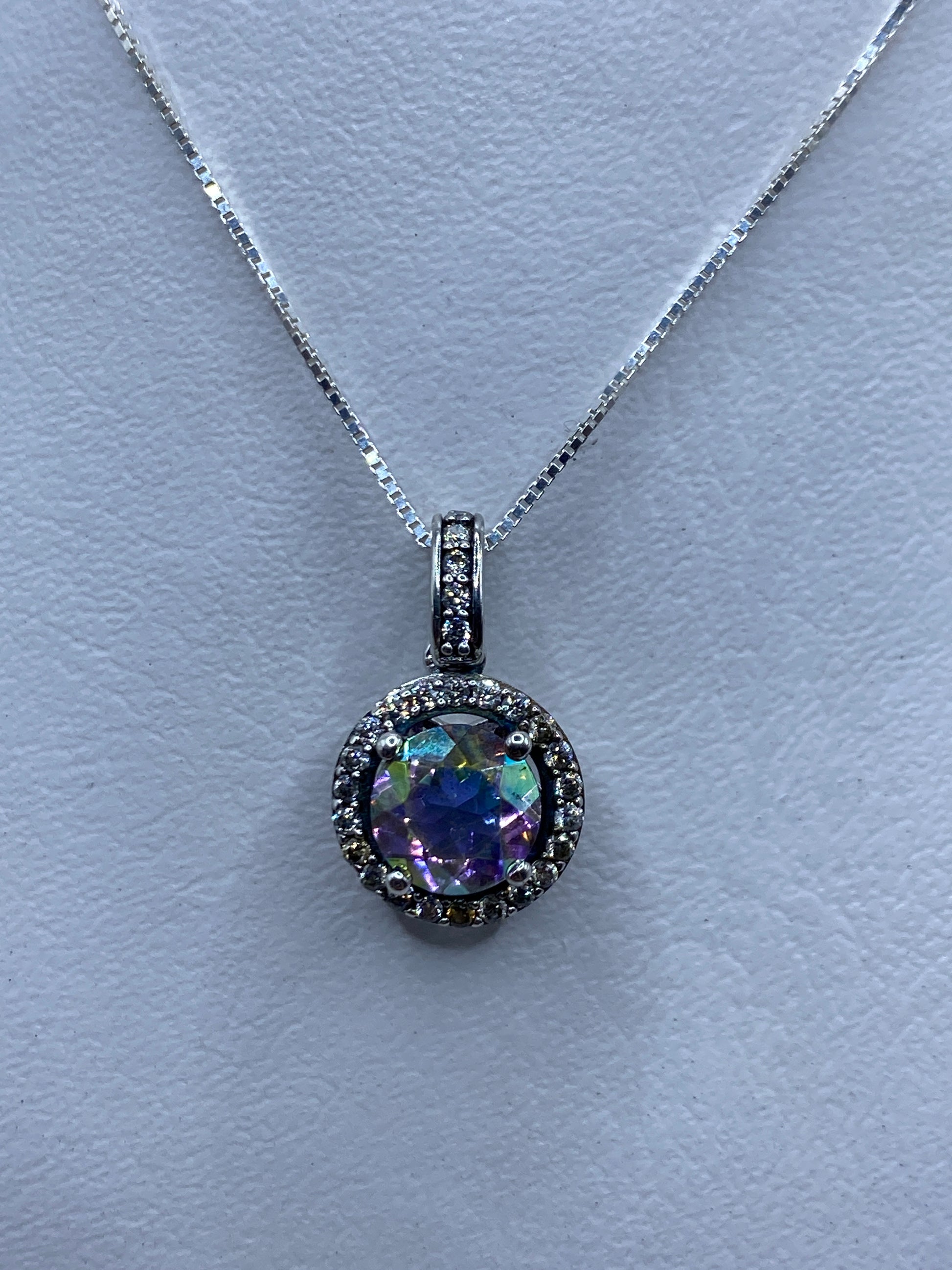 Dije de plata con circonia multicolor facetada, colgado de cadena, reflejando luz en tonos púrpura, verde y azul