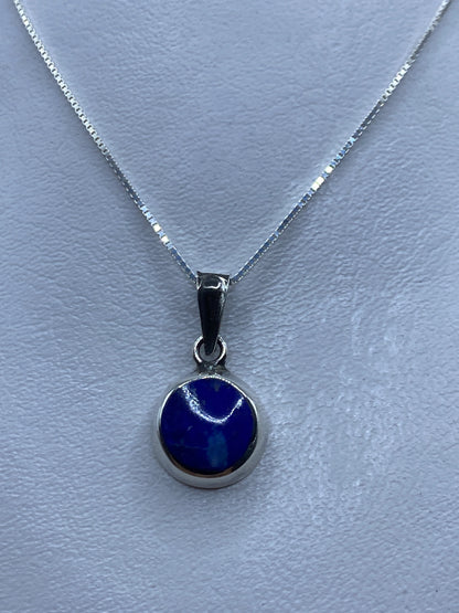 Dije de plata .925 con piedra azul engastada, colgando de cadena de plata sobre fondo azul