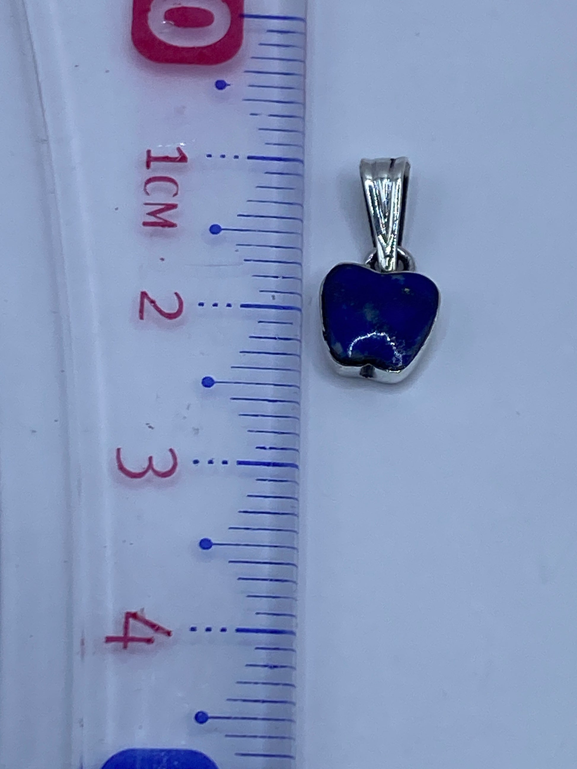 Dije de corazón azul con cierre de argolla de plata, junto a regla de medidas