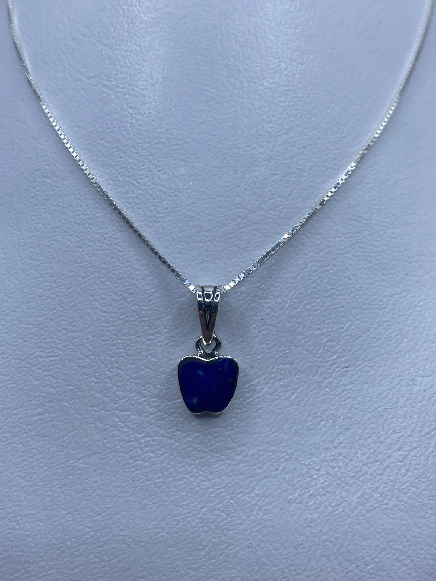 Dije de plata con piedra azul engastada, colgando de cadena delgada
