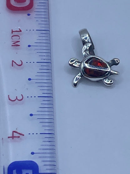 Dije tortuga sobre regla mostrando 2.6 cm de largo — tamaño compacto