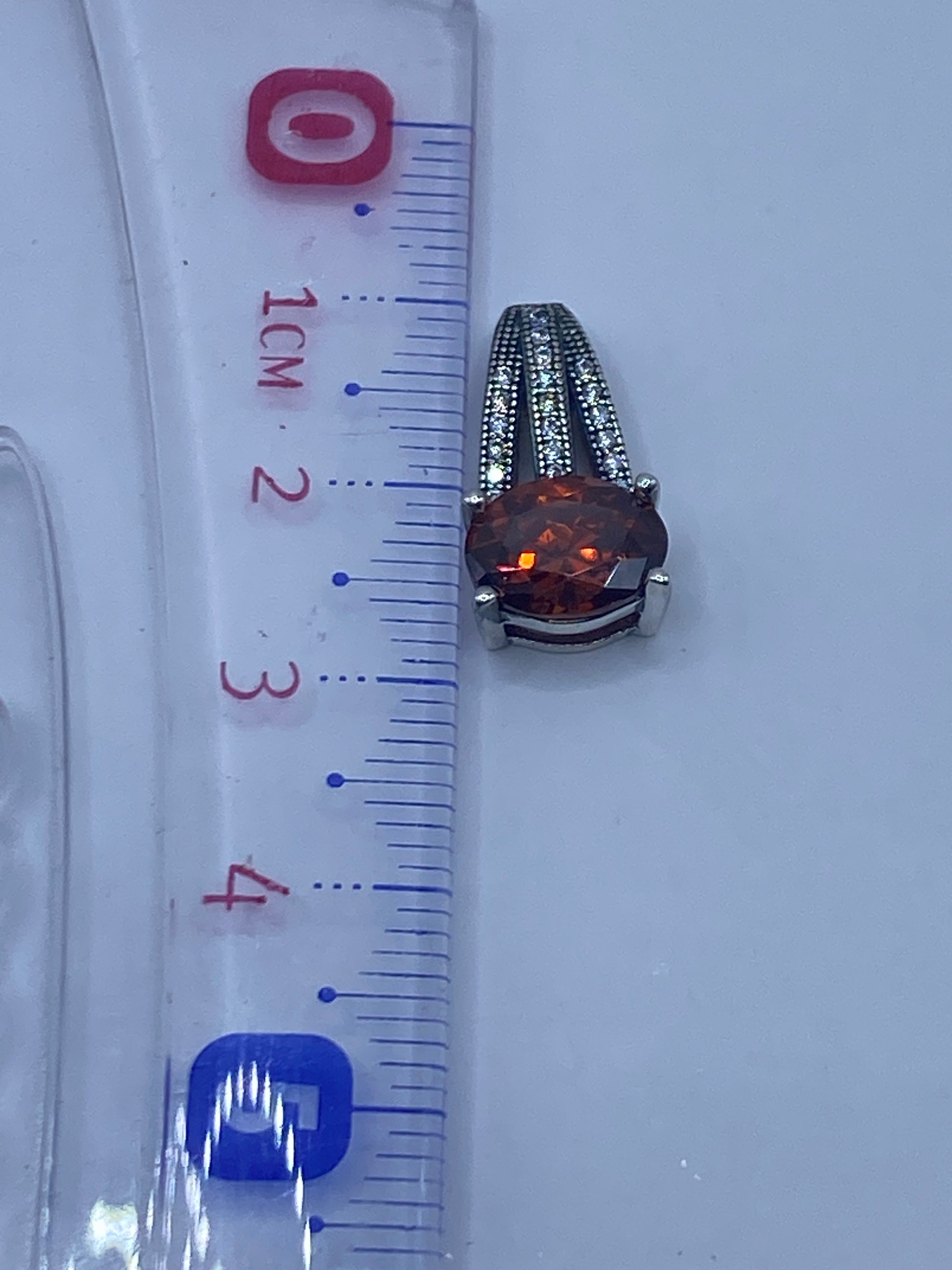 Dije en escala con regla midiendo 2.6 cm de largo, sin cadena