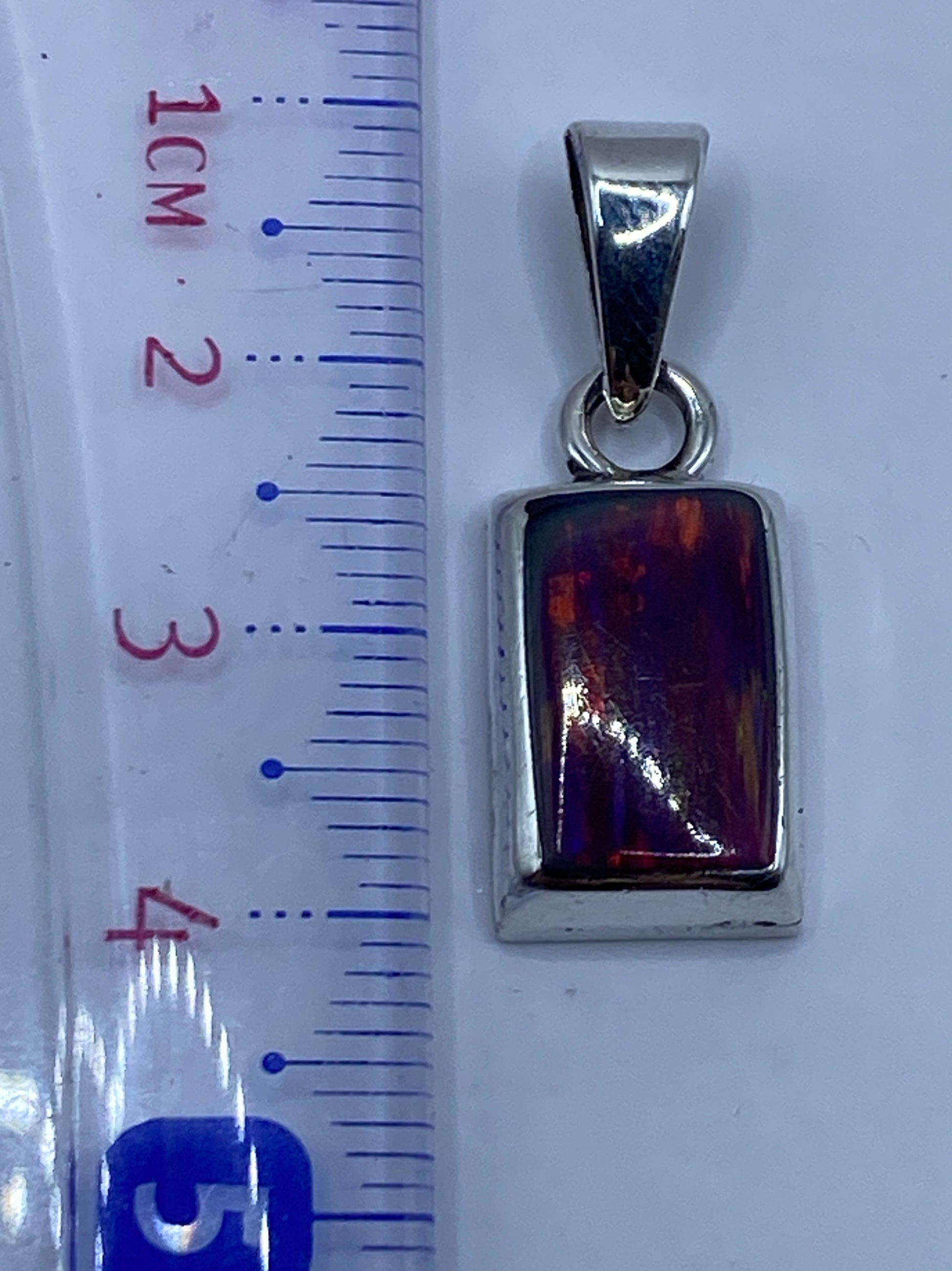 Dije de 3.8 cm junto a regla para referencia de tamaño, mostrando la piedra y engaste a mano
