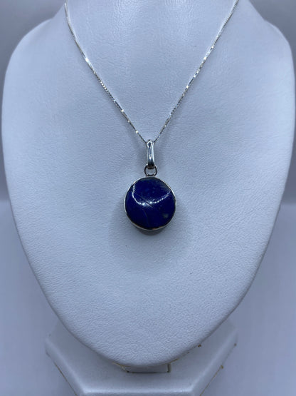 Dije sobre fondo blanco — vista frontal de la piedra azul y el engaste