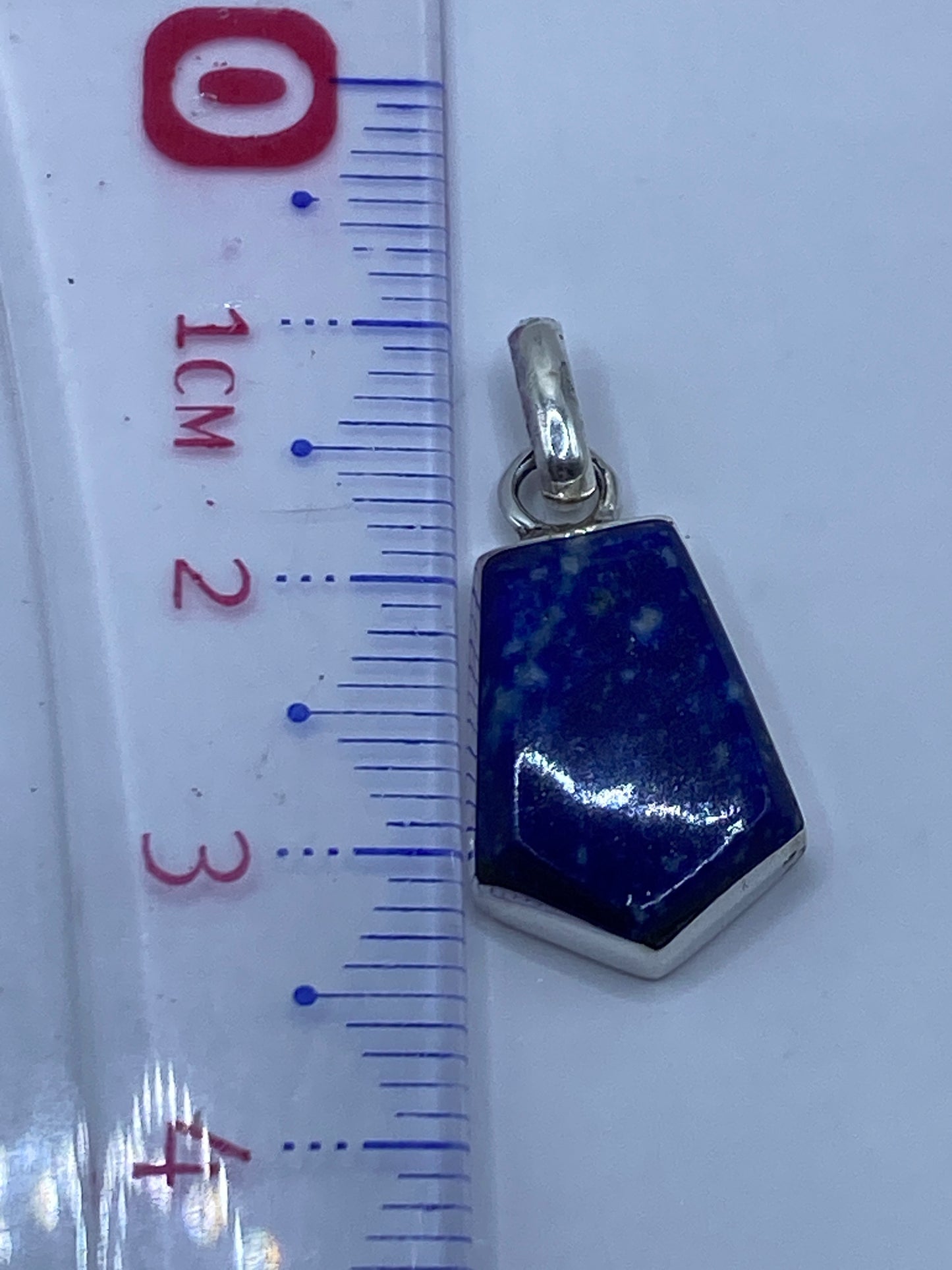 Dije de plata con piedra azul en la mano mostrando proporción
