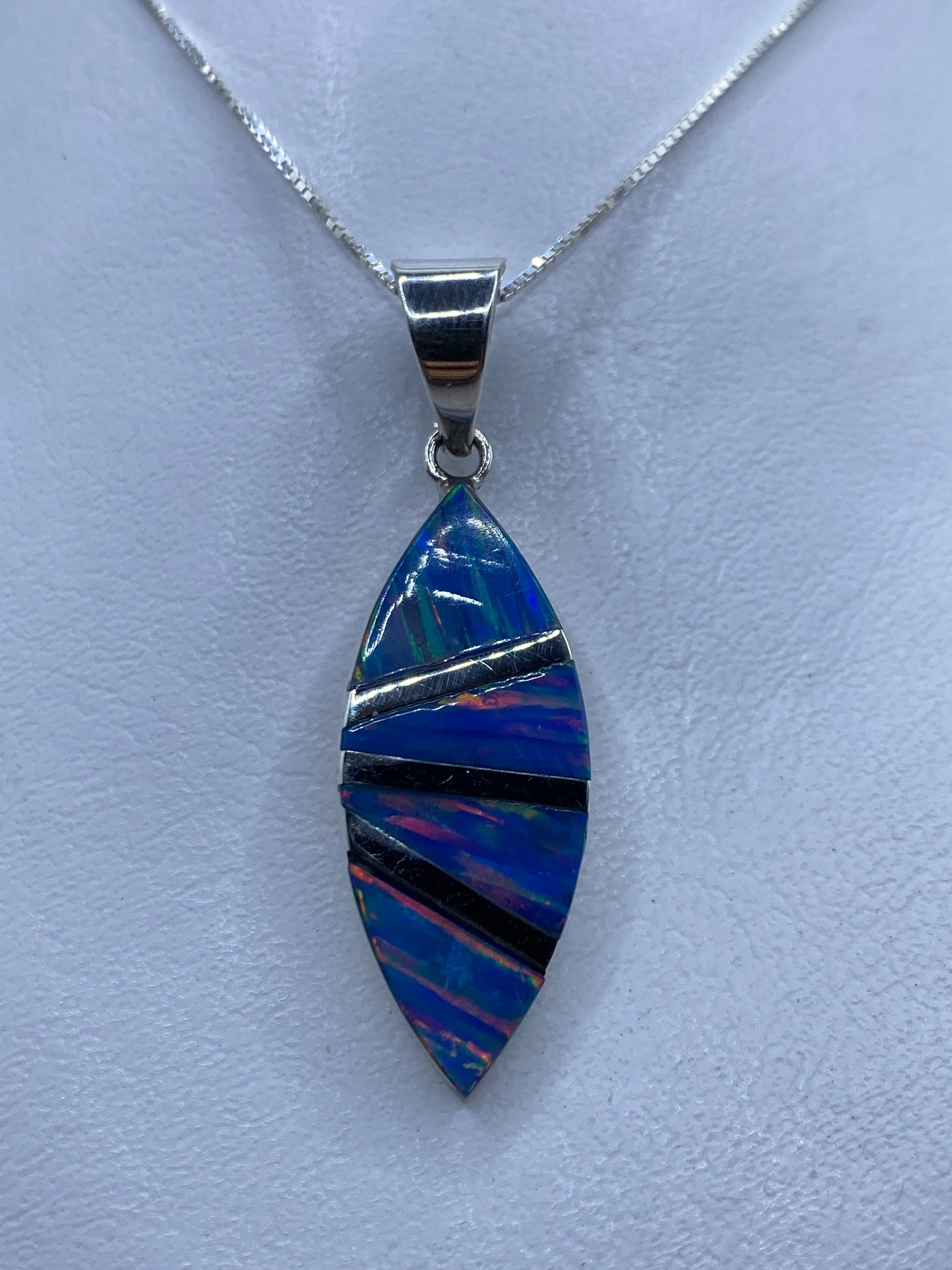 Dije de plata con ópalo de fuego azul incrustado a mano, colgando de cadena en cuello